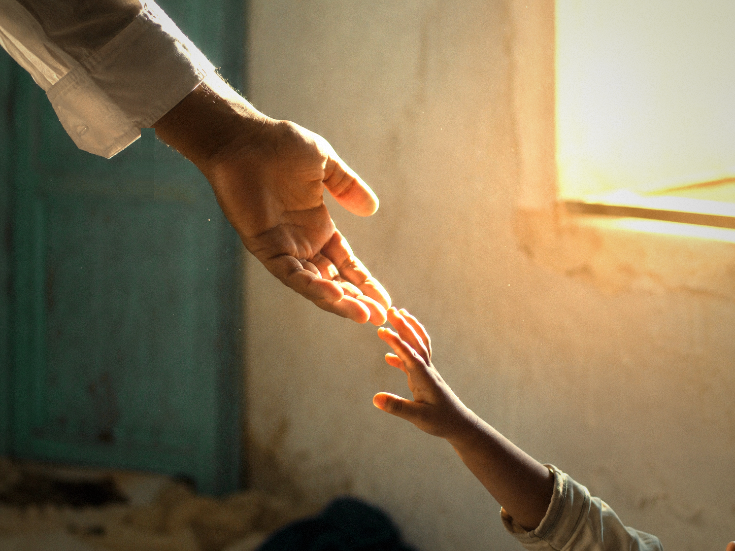 La main d'un adulte tendue vers celle d'un enfant dans la lumière